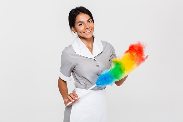Vrolijke brunette huishoudster in uniform houden kleurrijke stofdoek