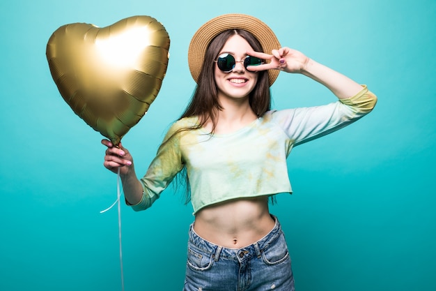 Vrolijke brunette mooie dame in jurk met gouden luchtballon als hart en geïsoleerd vredesgebaar tonen