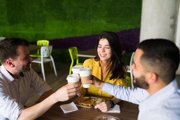 Vrolijke collega's juichen en toasten met koffie terwijl ze samen lunchen op de food court na het verlaten van het kantoor