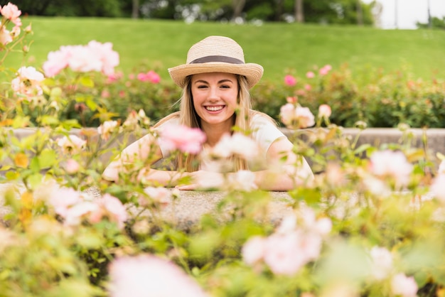 Vrolijke dame in hoed dichtbij witte bloei in park