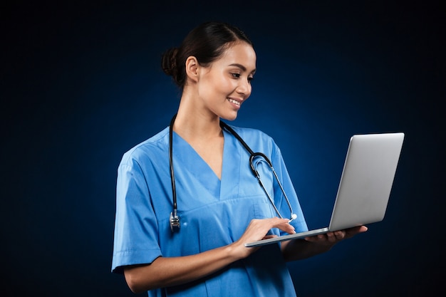 Vrolijke dame in medisch uniform met behulp van laptop