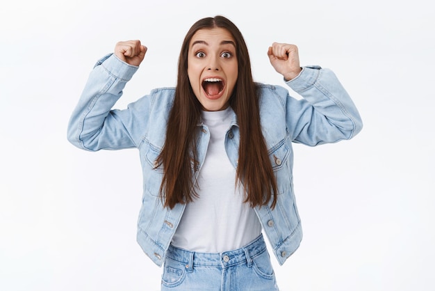 Gratis foto vrolijke en opgewonden vrouw juichen triomferen als het ontvangen van award schreeuwen van geluk en opgetogen handen opsteken vieren overwinning winnaar of kampioen staande witte achtergrond