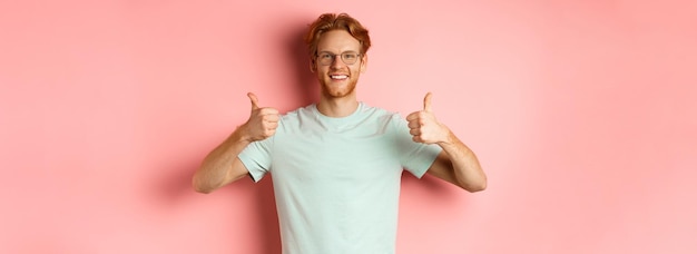 Gratis foto vrolijke europese man met rood haar en baard met een bril die duim omhoog laat zien en goedkeurend glimlacht