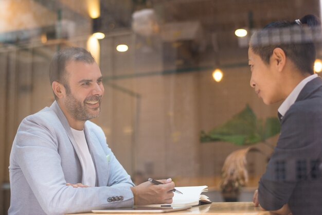 Vrolijke gelukkige h-manager die aan vrouwelijke kandidaat in koffie spreekt