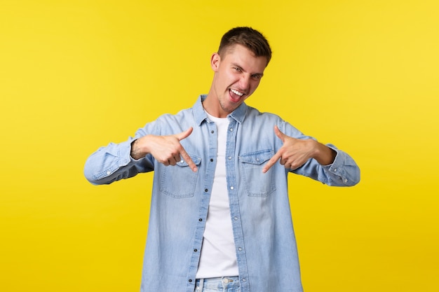 Vrolijke, gelukkige mannelijke student in vrijetijdskleding raadt aan om zich aan te melden voor taalcursussen, met de vingers naar beneden te wijzen op banner, opgewonden glimlachend, uitnodigend voor een evenement, goede aanbieding te promoten, gele achtergrond