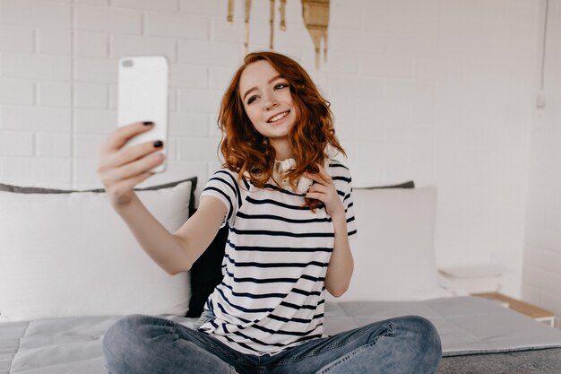 Vrolijke gembervrouw die foto van zichzelf neemt. Debonair jonge dame met behulp van telefoon voor selfie.
