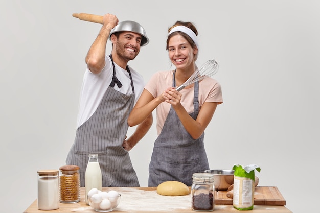 Vrolijke getrouwde vrouw en man hebben kookles, vechten met keukenbenodigdheden, genieten van favoriete hobby thuis, nemen deel aan een culinaire show, maken deeg om heerlijk eten te bakken of pannenkoeken te maken.