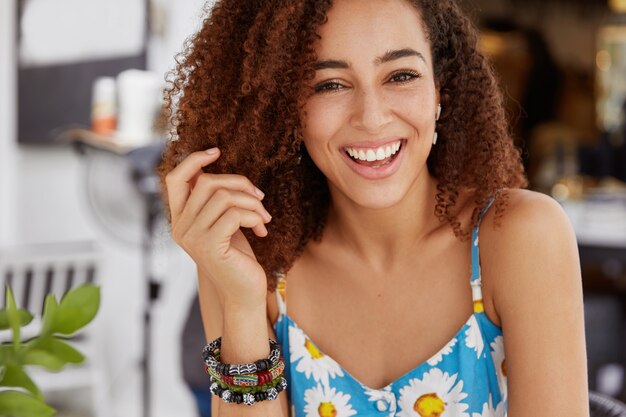 Vrolijke glimlachende donkere vrouw met borstelig kapsel, draagt een zomert-shirt en een armband
