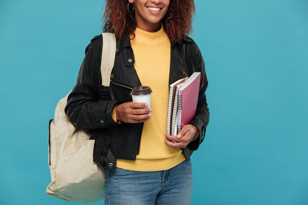 Vrolijke jonge Afrikaanse vrouw met notebooks en koffie.