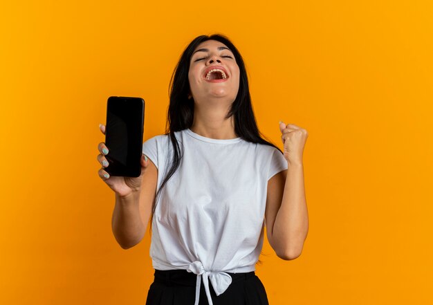 Vrolijke jonge blanke vrouw houdt telefoon vast en houdt vuist