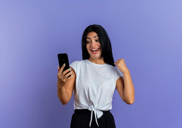 Vrolijke jonge blanke vrouw houdt vuist en kijkt naar de telefoon