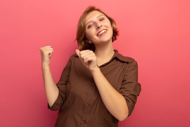 Vrolijke jonge blonde vrouw kijkt naar voren wijzend achter geïsoleerd op roze muur met kopieerruimte copy