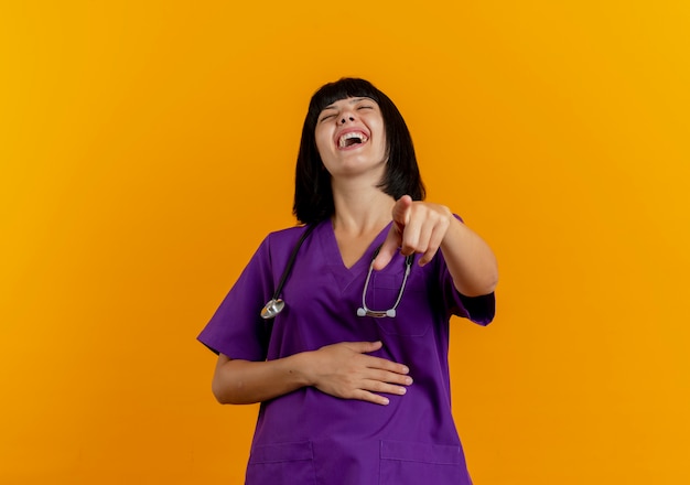 Vrolijke jonge brunette vrouwelijke arts in uniform met stethoscoop lachen