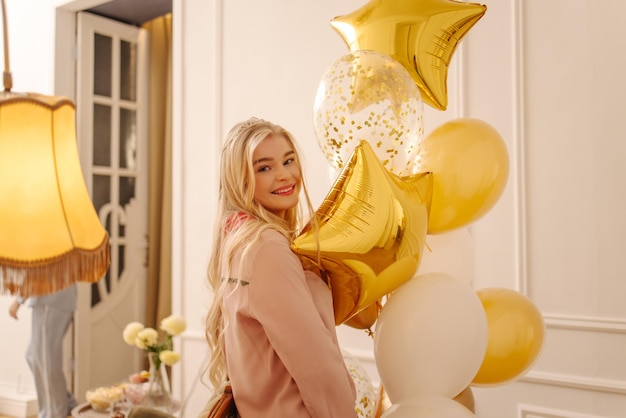 Vrolijke jonge Europese blonde vrouw vol goede moed poseren met ballonnen op pyjama party Vakantie concept