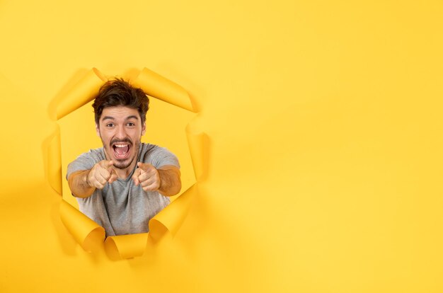 Vrolijke jonge man die kijkt van gescheurde gele papieren achtergrond verkoop man binnen gezichtsbehandeling