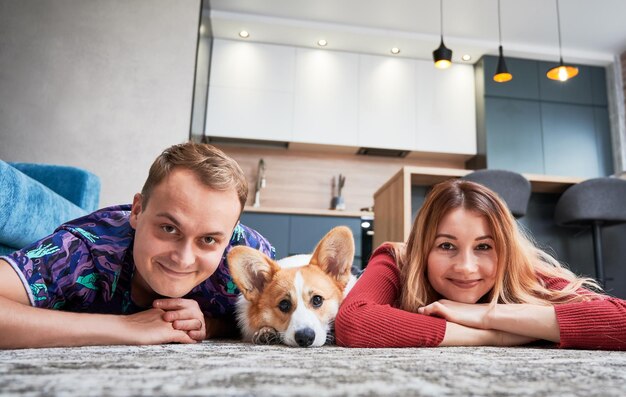 Vrolijke jonge man en vrouw die op de vloer liggen met schattige Corgi