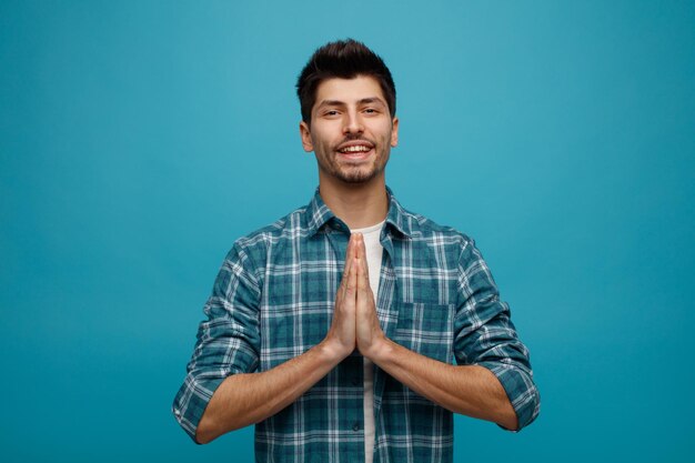 Vrolijke jonge man kijken camera met namaste gebaar geïsoleerd op blauwe achtergrond