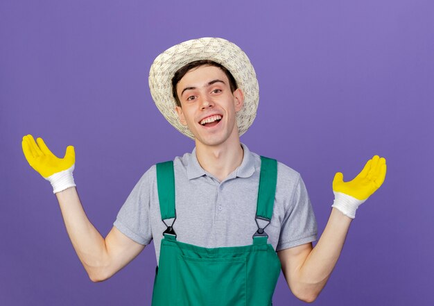Vrolijke jonge mannelijke tuinman met tuinhoed en handschoenen staat met open handen
