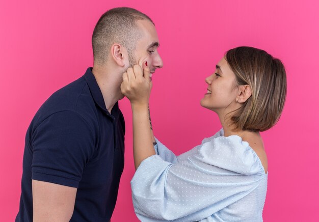 Vrolijke jonge mooie paar lachende vrouw knijpen wangen van haar mooie vriendje staande over roze muur