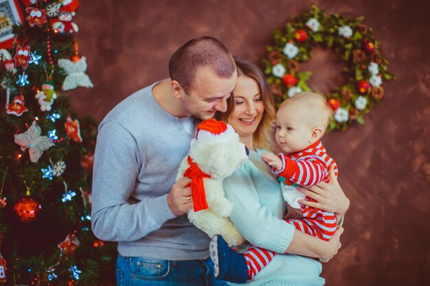 Vrolijke jonge ouders houden een klein kind poseren voor een kerstboom