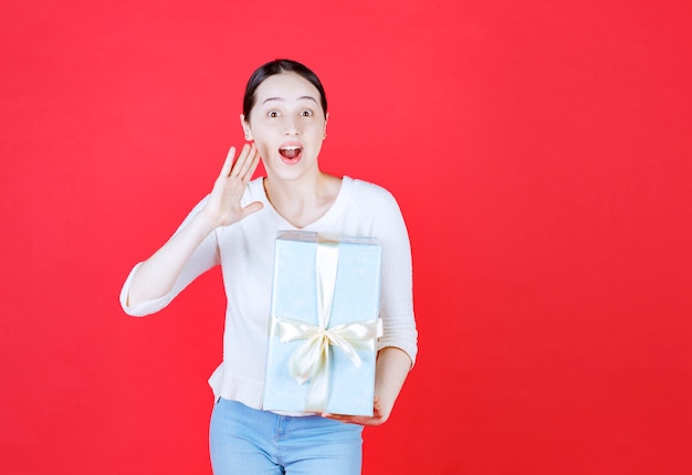 Vrolijke jonge vrouw die een geschenkdoos vasthoudt en iets zegt