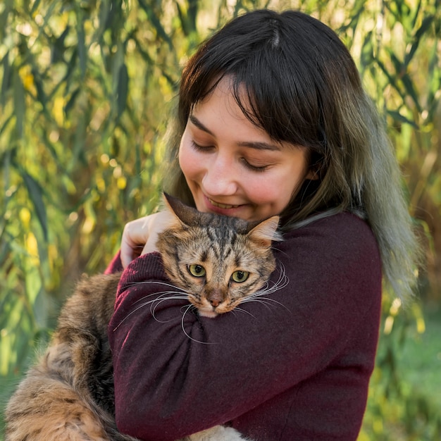 Gratis foto vrolijke jonge vrouw die van haar gestreepte katkat in tuin houden