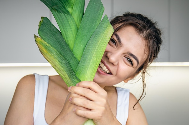 Vrolijke jonge vrouw in de keuken houdt een prei in haar handen