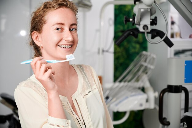 Vrolijke jonge vrouw met beugels op tanden met tandenborstel