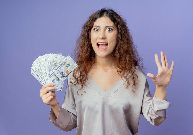 vrolijke jonge vrouw met contant geld en gespreide hand geïsoleerd op blauw