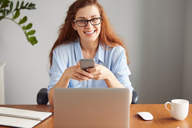 Vrolijke jonge zakenvrouw die op laptop werkt terwijl ze op haar werkplek zit