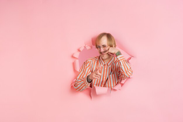 Vrolijke jongeman poseert in een gescheurde muur van koraalpapier, emotioneel en expressief