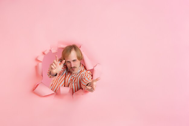 Vrolijke jongeman poseert in een gescheurde muur van koraalpapier, emotioneel en expressief