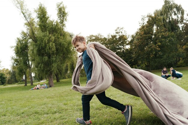 Vrolijke jongen die met een vliegende deken in het park loopt