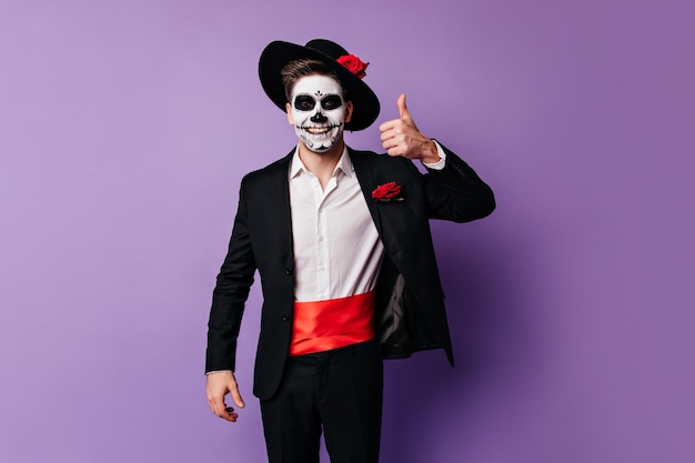 Vrolijke kerel in goed humeur verschijnt duim, poseren in kostuum voor feest op Halloween.
