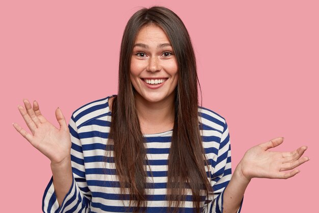 Vrolijke knappe jonge blanke vrouw met lang donker steil haar, voelt zich verbaasd over wat ze wil