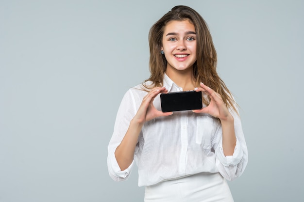 Vrolijke leuke vrouw die vinger op het smartphonescherm richten dat op een witte achtergrond wordt geïsoleerd.