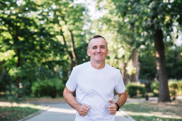 Vrolijke man in witte t-shirt die in een park loopt