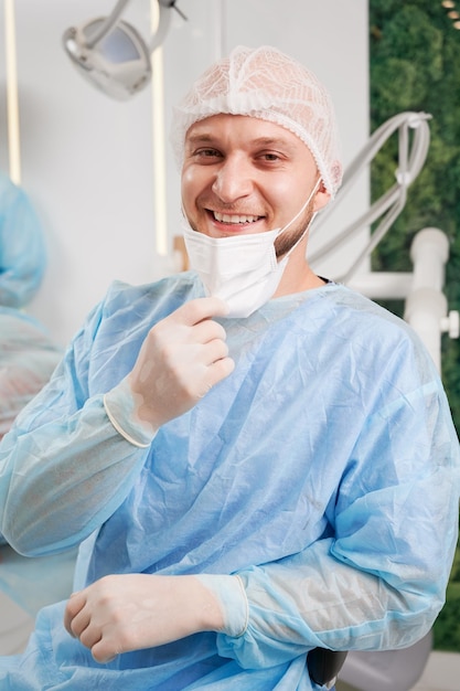 Vrolijke mannelijke tandarts zit in tandartspraktijk
