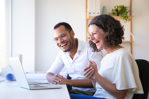 Vrolijke medewerkers kijken naar laptop en lachen