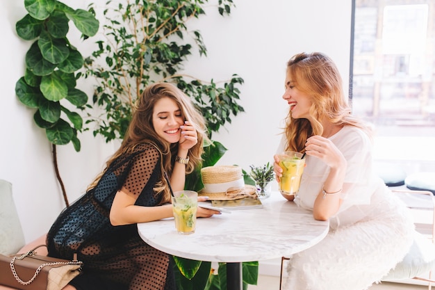 Vrolijke meisjes in elegante jurken en trendy accessoires die tijd doorbrengen en iets leuks bespreken