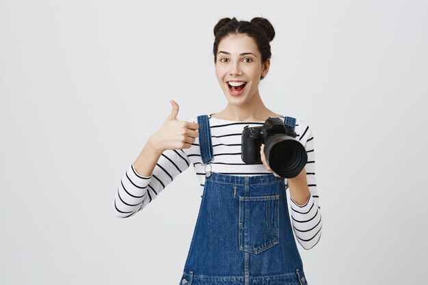 Vrolijke meisjesfotograaf die thumbs-up toont, goed werk van model prijst, compliment maakt