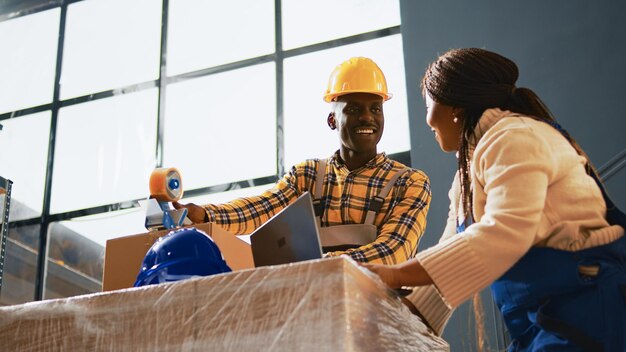 Vrolijke mensen die samen plezier hebben in het magazijn, werken aan de productie van producten en voorraadproductie. Team van arbeiders die lachen en verzending met goederen plannen. Schot uit de hand.