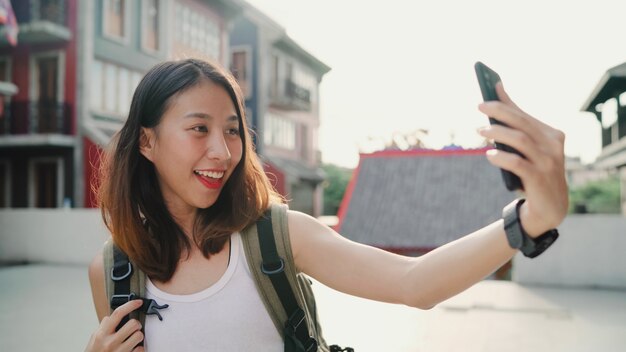 Vrolijke mooie jonge Aziatische backpacker blogger vrouw met behulp van smartphone selfie te nemen