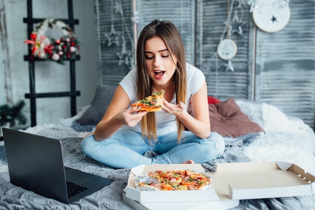 Vrolijke mooie vrouw bestelde pizza naar huis. vrouw die in bed eet. lekkere italiaanse hapjes.