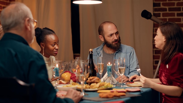 Vrolijke multi-etnische mensen in de eetkamer die de wintervakantie vieren met traditioneel huisgemaakt voedsel. Gelukkige feestelijke familie die thuis geniet van het kerstdiner terwijl ze samen eten. Uit de hand geschoten