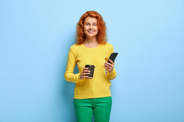 Vrolijke roodharige student moderne mobiele telefoon in handen houdt, geniet van chatten met vriend via applicatie