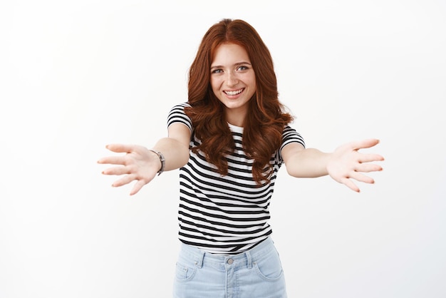 Vrolijke roodharige vrouw in gestreepte tshirt leun naar voren armen uitstrekken wil vasthouden of iets in haar armen hebben glimlachend vreugdevol knuffelen vriend groet met gastvrije omhelst witte achtergrond