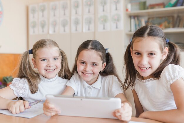Vrolijke schoolmeisjes met tablet camera kijken