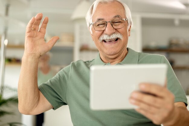 Vrolijke senior man die plezier heeft tijdens het gebruik van touchpad thuis