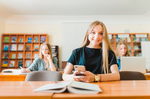 Vrolijke tiener met smartphone dichtbij handboek